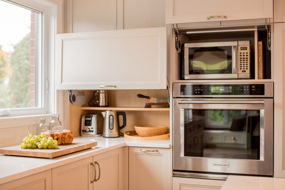 Example of a mid-sized transitional l-shaped medium tone wood floor and brown floor eat-in kitchen design in Montreal with an undermount sink, recessed-panel cabinets, white cabinets, quartz countertops, white backsplash, ceramic backsplash, paneled appliances and an island