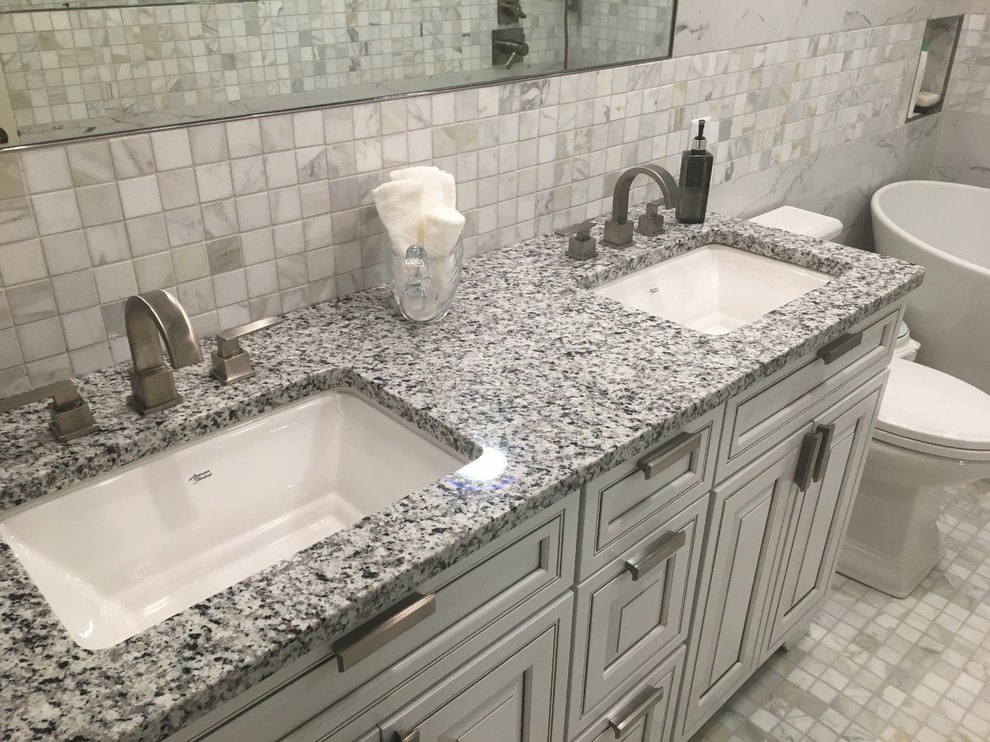 Photo of a mid-sized transitional master bathroom in Other with raised-panel cabinets, white cabinets, a freestanding tub, a two-piece toilet, gray tile, white tile, marble, grey walls, marble floors, an undermount sink, granite benchtops, grey floor and grey benchtops.