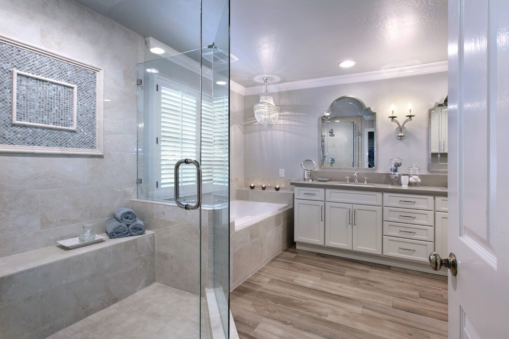 This is an example of a mid-sized transitional master bathroom in Orange County with shaker cabinets, white cabinets, a drop-in tub, a corner shower, a one-piece toilet, beige tile, stone tile, grey walls, porcelain floors, an undermount sink, engineered quartz benchtops and beige floor.
