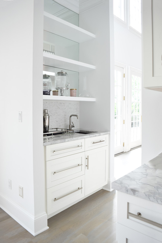 This is an example of a large beach style l-shaped eat-in kitchen in New York with an undermount sink, shaker cabinets, white cabinets, quartzite benchtops, grey splashback, marble splashback, stainless steel appliances, light hardwood floors and with island.