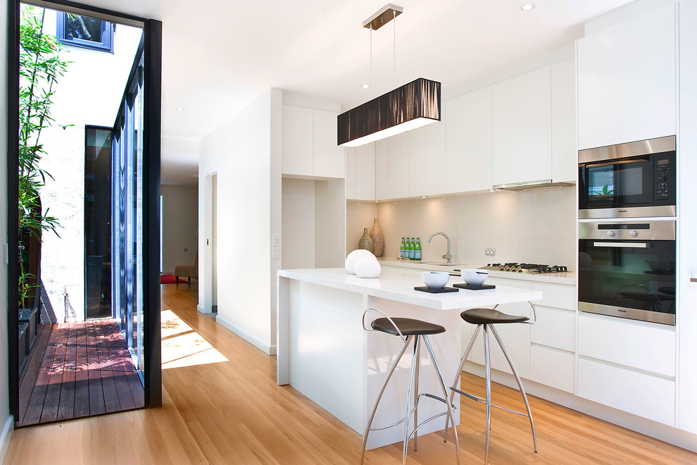 Contemporary l-shaped kitchen in Sydney with flat-panel cabinets, white cabinets, beige splashback, stainless steel appliances and with island.