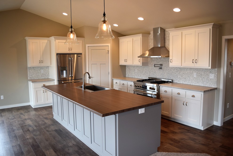 Open concept kitchen - large medium tone wood floor open concept kitchen idea with a drop-in sink, recessed-panel cabinets, white cabinets, laminate countertops, multicolored backsplash, ceramic backsplash, stainless steel appliances and an island