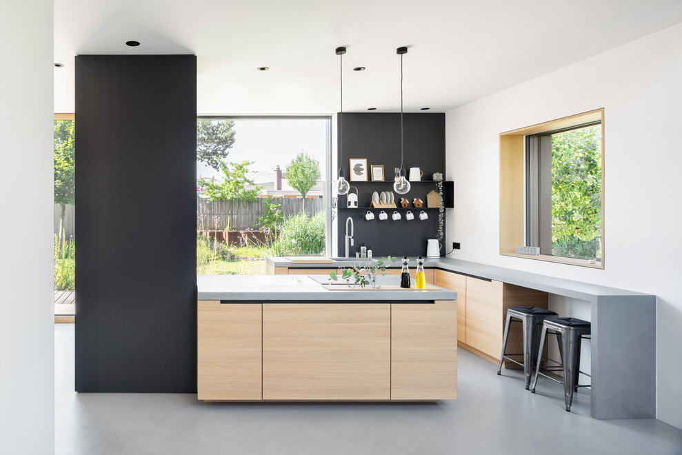 This is an example of a scandinavian open plan kitchen in Munich with flat-panel cabinets, light wood cabinets, concrete benchtops, black splashback, concrete floors, grey benchtop, a single-bowl sink and grey floor.