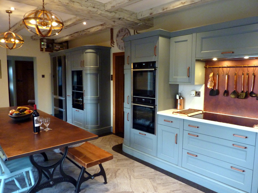Inredning av ett klassiskt stort vit vitt kök, med en rustik diskho, luckor med profilerade fronter, blå skåp, bänkskiva i kvartsit, orange stänkskydd, svarta vitvaror, vinylgolv, en köksö och grått golv