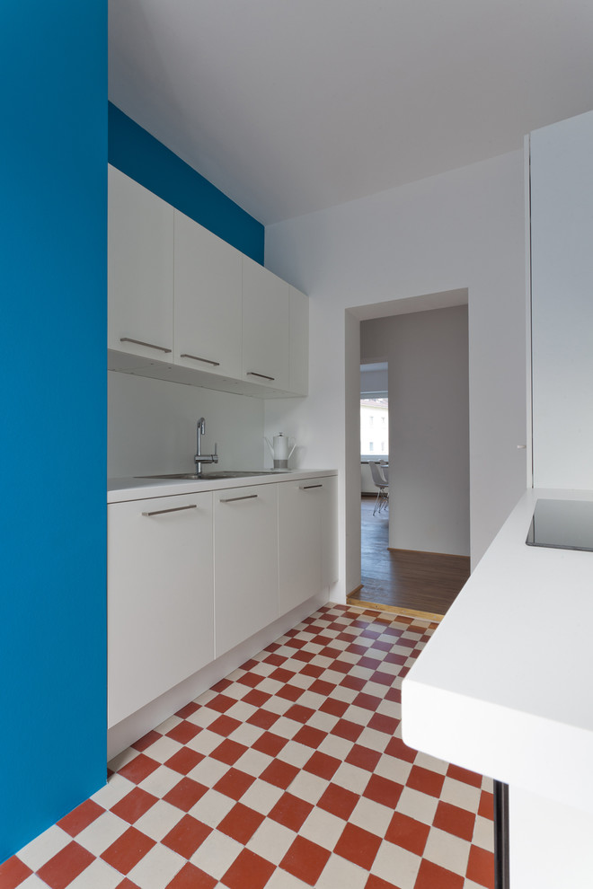 Design ideas for a small contemporary galley separate kitchen in Frankfurt with a drop-in sink, flat-panel cabinets, white cabinets, blue splashback, glass sheet splashback, porcelain floors and no island.