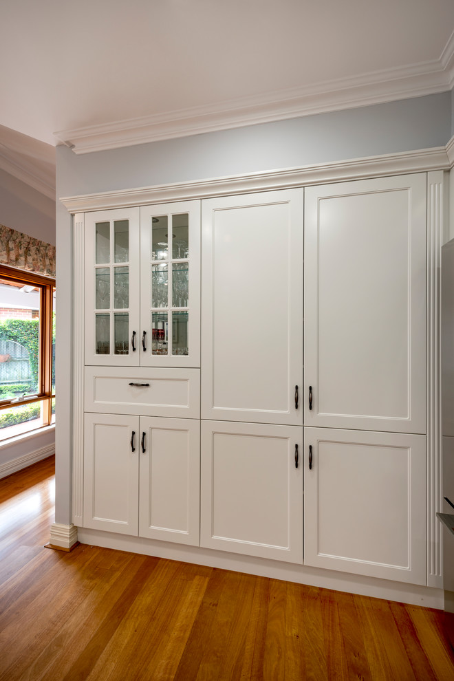 Mid-sized traditional u-shaped separate kitchen in Perth with a drop-in sink, recessed-panel cabinets, white cabinets, granite benchtops, white splashback, porcelain splashback, black appliances, light hardwood floors, a peninsula, yellow floor and black benchtop.