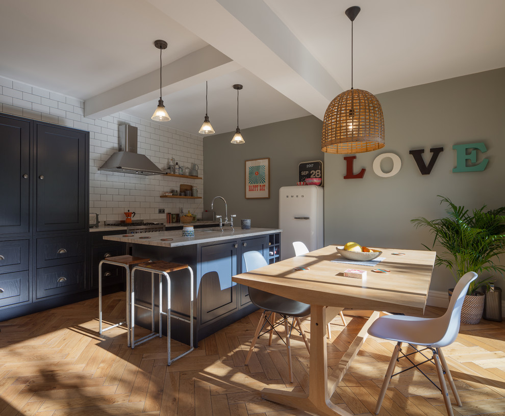 This is an example of a contemporary galley eat-in kitchen in Manchester with a drop-in sink, shaker cabinets, grey cabinets, white splashback, ceramic splashback, light hardwood floors and with island.