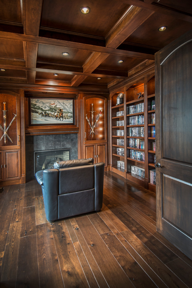 This is an example of a mid-sized transitional enclosed family room in Omaha with a library, brown walls, dark hardwood floors, a standard fireplace, a tile fireplace surround and brown floor.