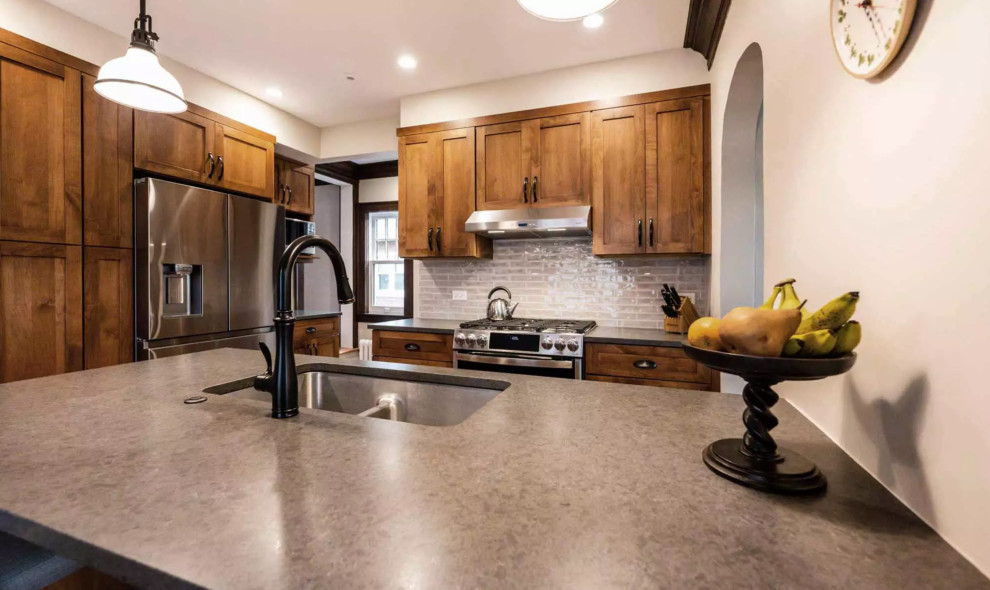 Example of a small mountain style galley medium tone wood floor and brown floor eat-in kitchen design with a drop-in sink, flat-panel cabinets, dark wood cabinets, gray backsplash, glass tile backsplash, stainless steel appliances, an island and gray countertops