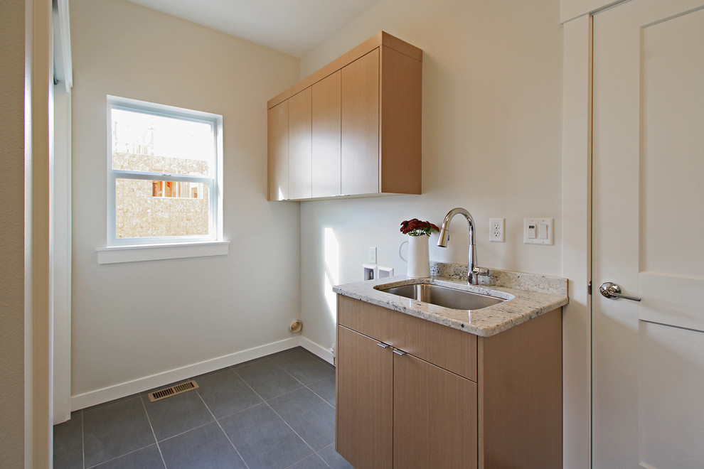 This is an example of a mid-sized arts and crafts galley utility room in Seattle with an undermount sink, flat-panel cabinets, medium wood cabinets, granite benchtops, grey walls, porcelain floors and a side-by-side washer and dryer.