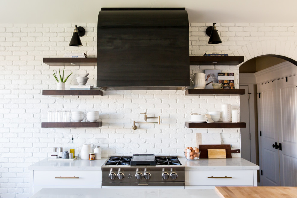 Inspiration for a mid-sized country l-shaped eat-in kitchen in Salt Lake City with a farmhouse sink, shaker cabinets, white cabinets, quartz benchtops, white splashback, brick splashback, black appliances, medium hardwood floors and with island.
