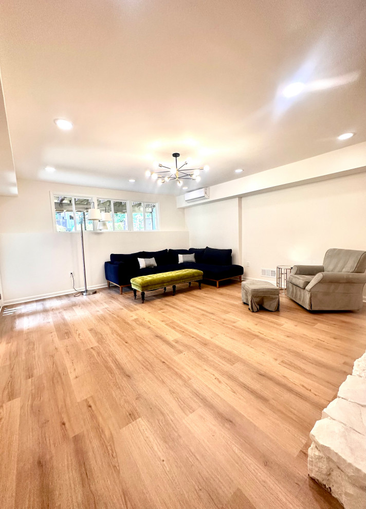 Cette photo montre un grand sous-sol moderne donnant sur l'extérieur avec salle de cinéma, un mur blanc, un sol en bois brun, une cheminée standard, un manteau de cheminée en bois, un sol marron et un plafond voûté.