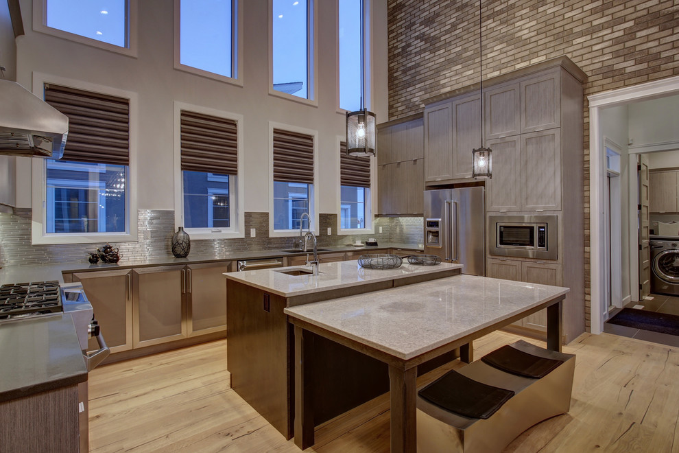 This is an example of a large contemporary galley eat-in kitchen in Calgary with stainless steel appliances, with island, a single-bowl sink, flat-panel cabinets, beige cabinets, quartzite benchtops, grey splashback, metal splashback, light hardwood floors and beige floor.