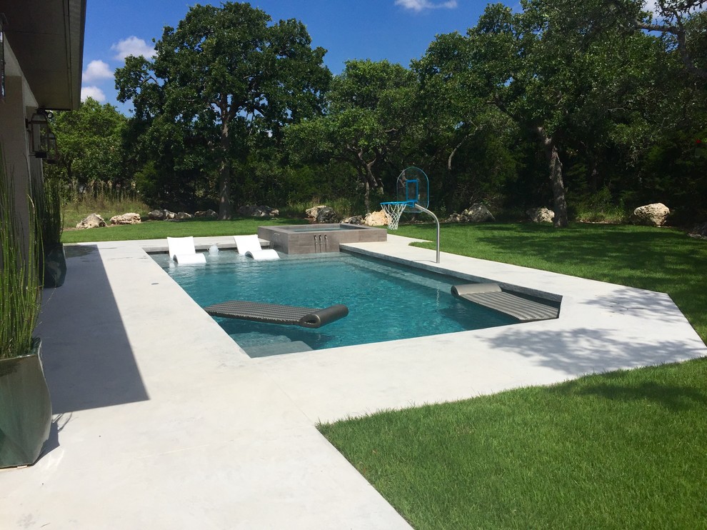 Inspiration for a mid-sized contemporary backyard custom-shaped lap pool in Houston with a hot tub and concrete slab.