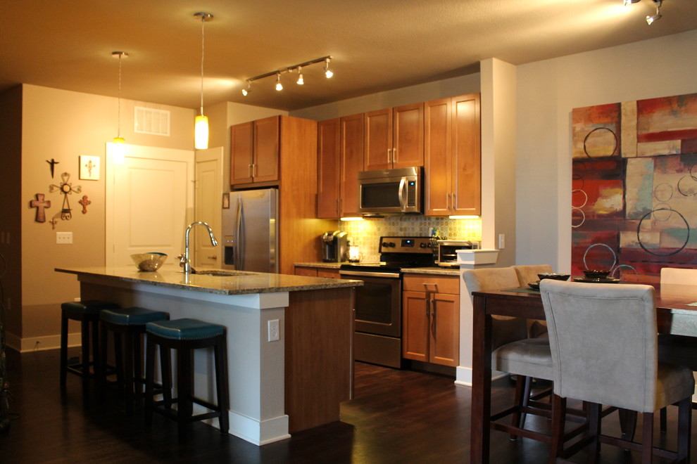 Photo of a small transitional single-wall kitchen in Dallas with a double-bowl sink, shaker cabinets, light wood cabinets, granite benchtops, multi-coloured splashback, stone tile splashback, stainless steel appliances, dark hardwood floors and with island.