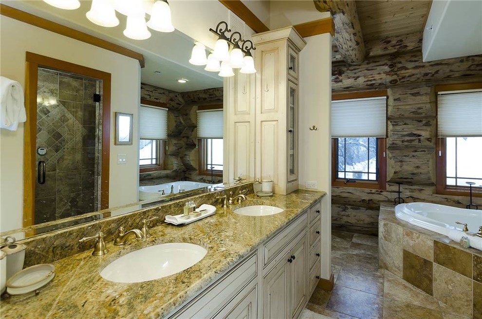 This is an example of a mid-sized transitional master bathroom in Denver with raised-panel cabinets, white cabinets, a drop-in tub, an alcove shower, a one-piece toilet, beige tile, brown tile, ceramic tile, brown walls, travertine floors, an undermount sink and granite benchtops.