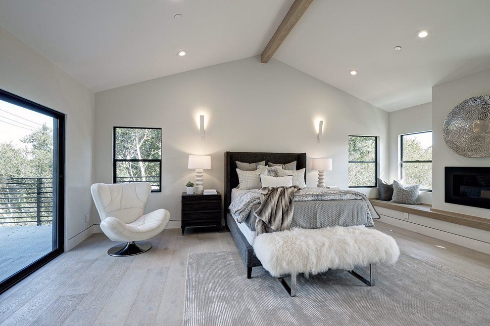 Photo of a large modern loft-style bedroom in San Francisco with white walls, light hardwood floors, a standard fireplace and beige floor.