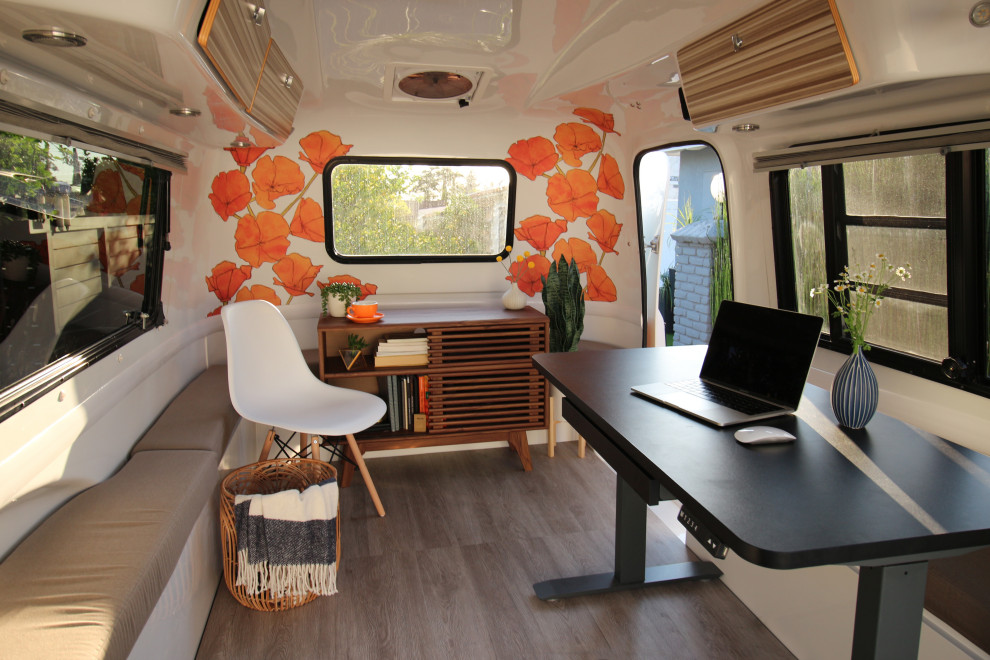 Immagine di un piccolo studio moderno con pareti arancioni, pavimento in laminato, scrivania autoportante, pavimento grigio e carta da parati