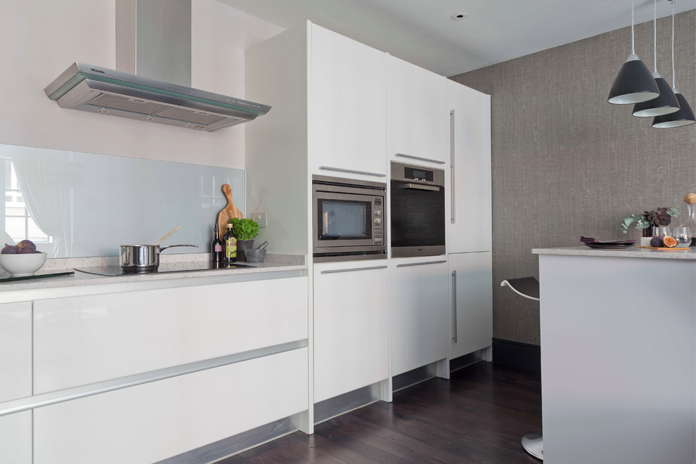Inspiration for a small contemporary galley eat-in kitchen in London with flat-panel cabinets, white cabinets, quartz benchtops, grey splashback, glass sheet splashback, stainless steel appliances, dark hardwood floors and with island.
