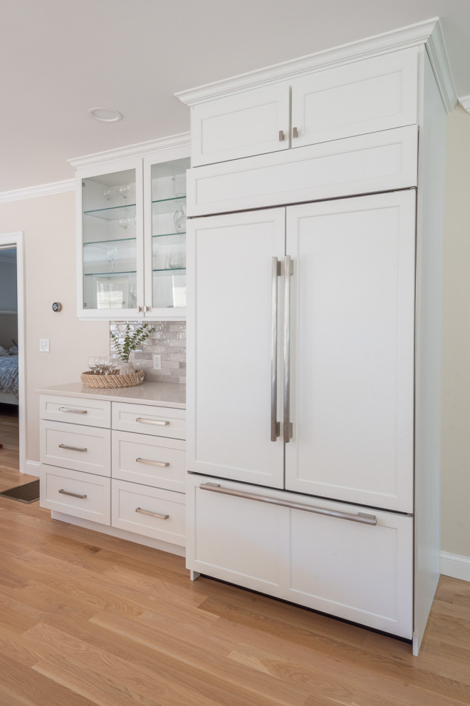 Example of a huge transitional l-shaped light wood floor and brown floor open concept kitchen design in Boston with an undermount sink, shaker cabinets, white cabinets, quartz countertops, gray backsplash, subway tile backsplash, stainless steel appliances, an island and white countertops
