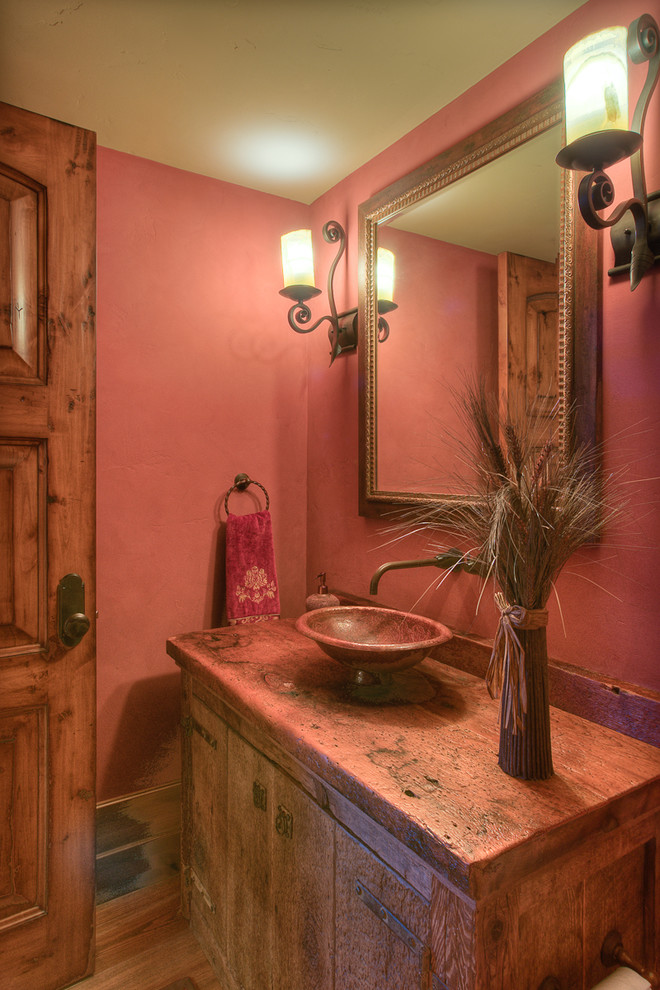 Mid-sized country powder room in Denver with a vessel sink, medium wood cabinets, medium hardwood floors and pink walls.