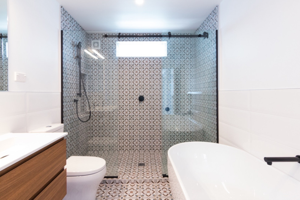 This is an example of a mid-sized contemporary master bathroom in Sydney with louvered cabinets, medium wood cabinets, a drop-in tub, an open shower, a one-piece toilet, black and white tile, mosaic tile, multi-coloured walls, an integrated sink, engineered quartz benchtops, multi-coloured floor, a hinged shower door, white benchtops, a single vanity and a floating vanity.