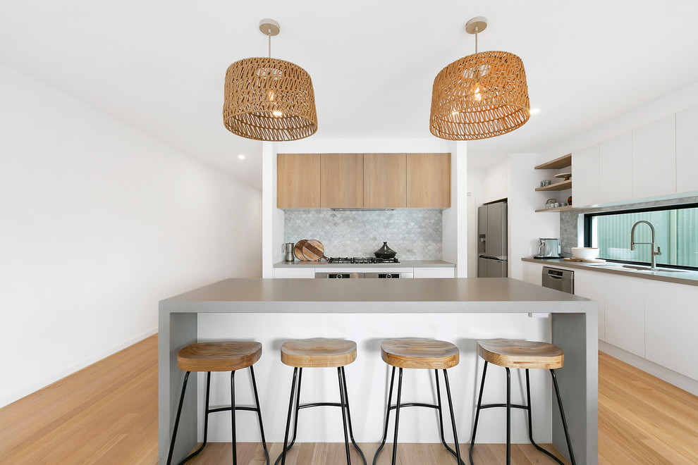 Contemporary u-shaped open plan kitchen in Melbourne with an undermount sink, flat-panel cabinets, white cabinets, quartz benchtops, grey splashback, stone tile splashback, stainless steel appliances, medium hardwood floors, with island and grey benchtop.