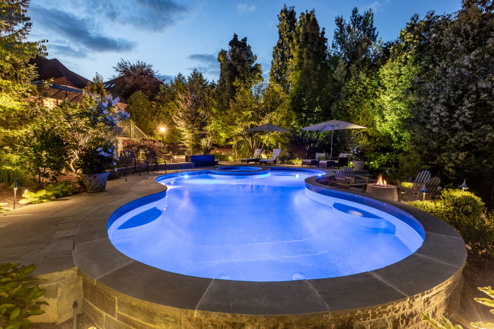 Modelo de piscina clásica de tamaño medio tipo riñón en patio trasero con paisajismo de piscina y adoquines de piedra natural