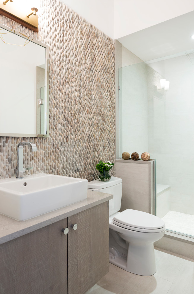 Mid-sized beach style 3/4 bathroom in New York with flat-panel cabinets, beige cabinets, an alcove shower, pebble tile, beige walls, porcelain floors, a vessel sink, limestone benchtops, beige floor and a hinged shower door.