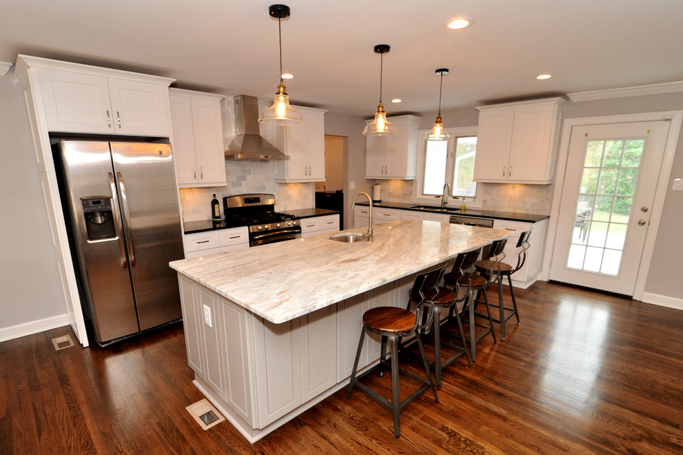 Inspiration for a mid-sized transitional l-shaped medium tone wood floor open concept kitchen remodel in Atlanta with a double-bowl sink, white cabinets, quartzite countertops, white backsplash, stainless steel appliances and an island