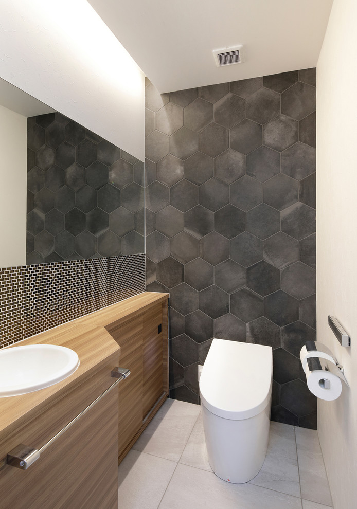 Mid-sized modern powder room in Tokyo with furniture-like cabinets, light wood cabinets, a one-piece toilet, black tile, porcelain tile, white walls, porcelain floors, a drop-in sink, laminate benchtops, grey floor and beige benchtops.