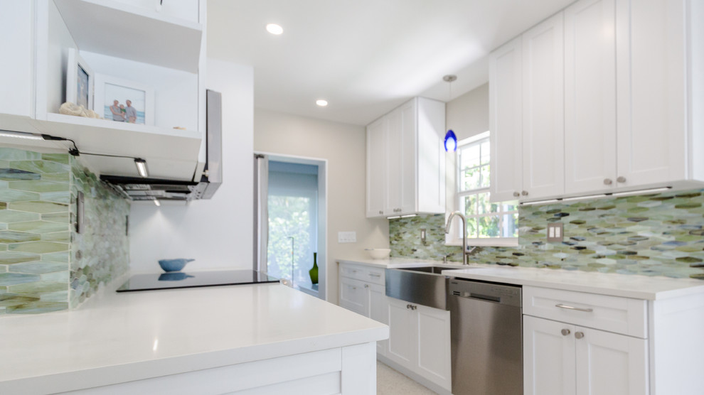 Mid-sized beach style l-shaped eat-in kitchen in Miami with a farmhouse sink, shaker cabinets, white cabinets, quartz benchtops, glass tile splashback, stainless steel appliances, no island, white floor, white benchtop, green splashback and terrazzo floors.