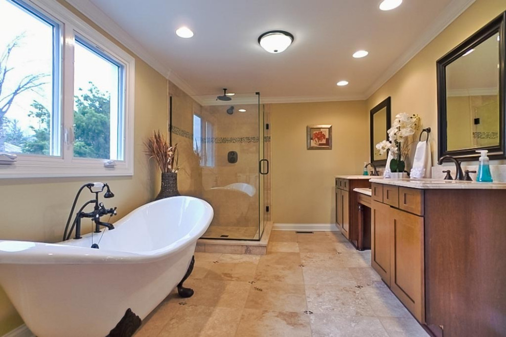 Photo of a midcentury master bathroom in Cleveland with shaker cabinets, medium wood cabinets, a claw-foot tub, a corner shower, beige tile, limestone, beige walls, limestone floors, an undermount sink, limestone benchtops, beige floor, a hinged shower door, multi-coloured benchtops, a double vanity and a freestanding vanity.
