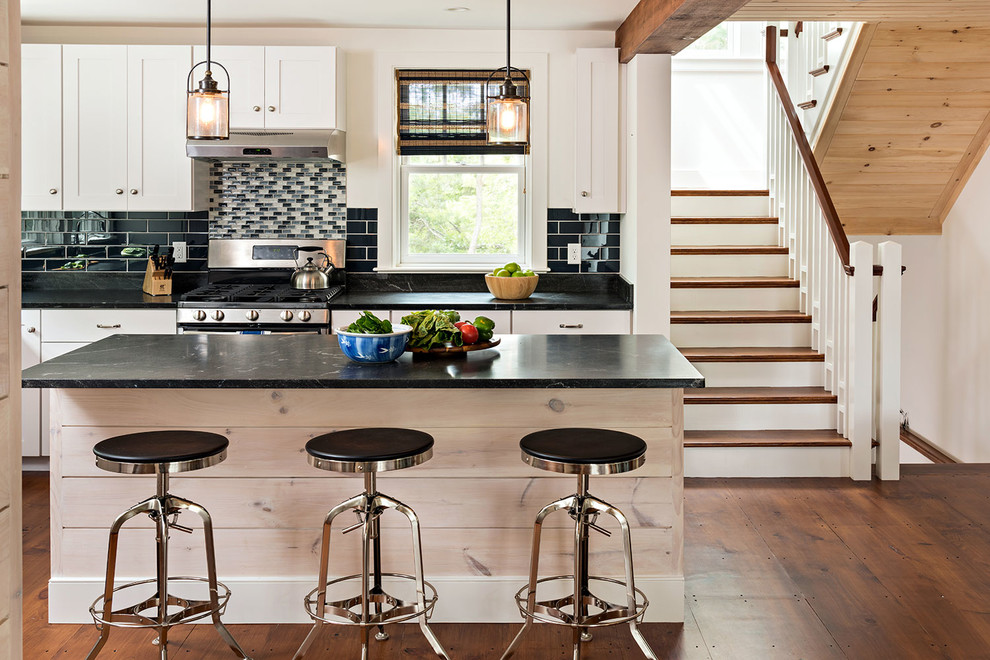 This is an example of a beach style kitchen in Boston with shaker cabinets, black splashback, subway tile splashback, stainless steel appliances, dark hardwood floors, with island, brown floor and black benchtop.