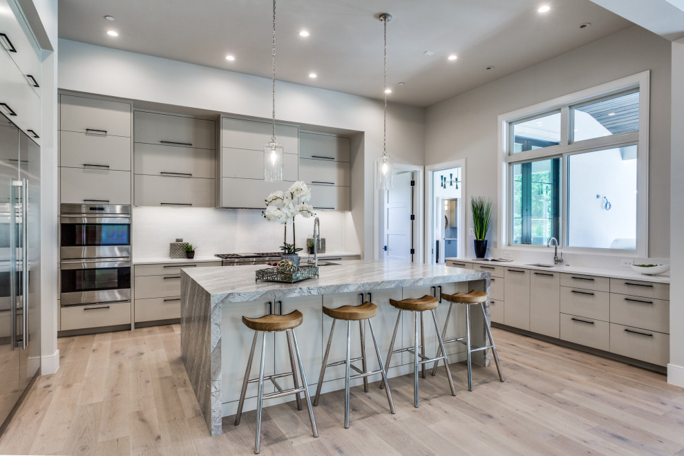 Inspiration for a large modern l-shaped kitchen in Dallas with a drop-in sink, flat-panel cabinets, white cabinets, marble benchtops, white splashback, stainless steel appliances, light hardwood floors, with island and multi-coloured benchtop.