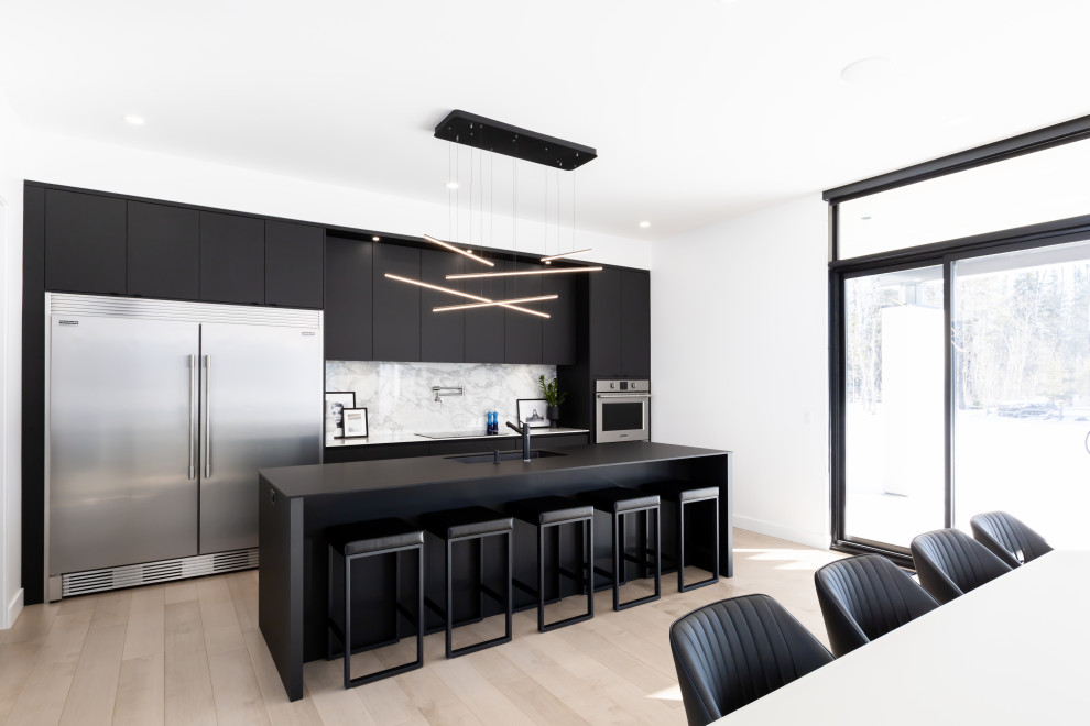 This is an example of a large modern galley open plan kitchen in New York with a double-bowl sink, flat-panel cabinets, black cabinets, quartz worktops, multi-coloured splashback, ceramic splashback, stainless steel appliances, light hardwood flooring, an island and black worktops.