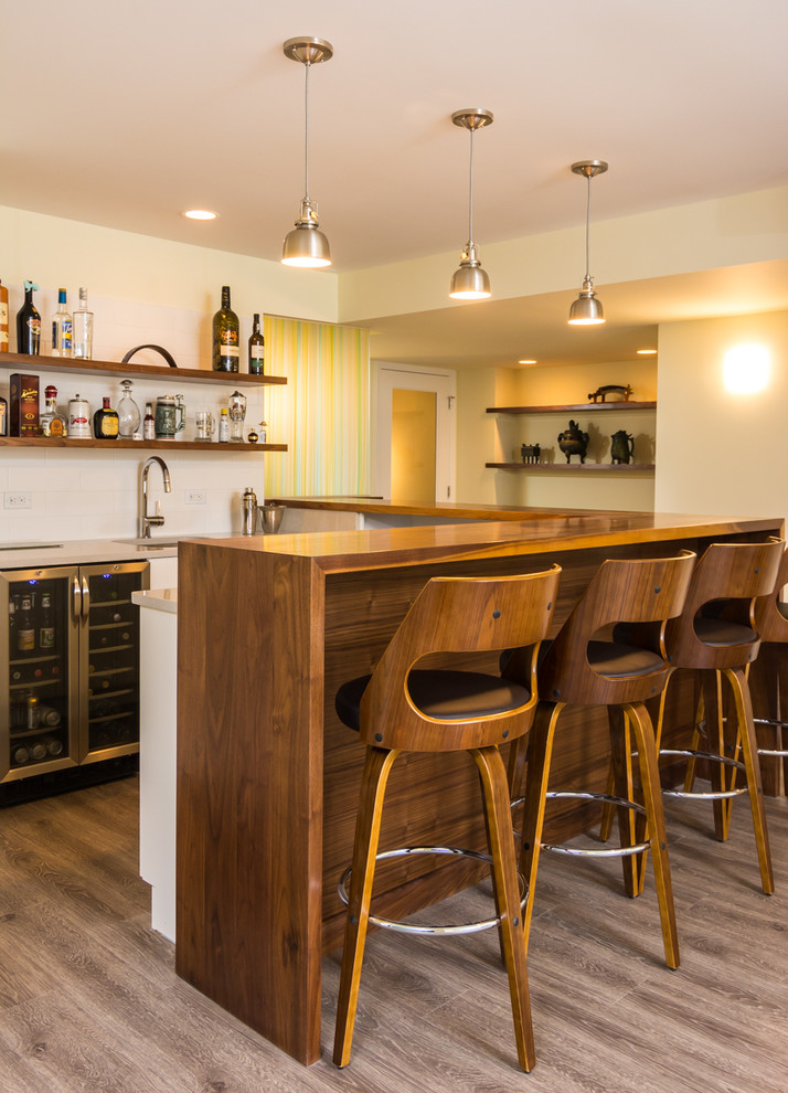 Photo of an expansive midcentury u-shaped seated home bar in Detroit with an undermount sink, wood benchtops, white splashback, subway tile splashback, brown floor and vinyl floors.