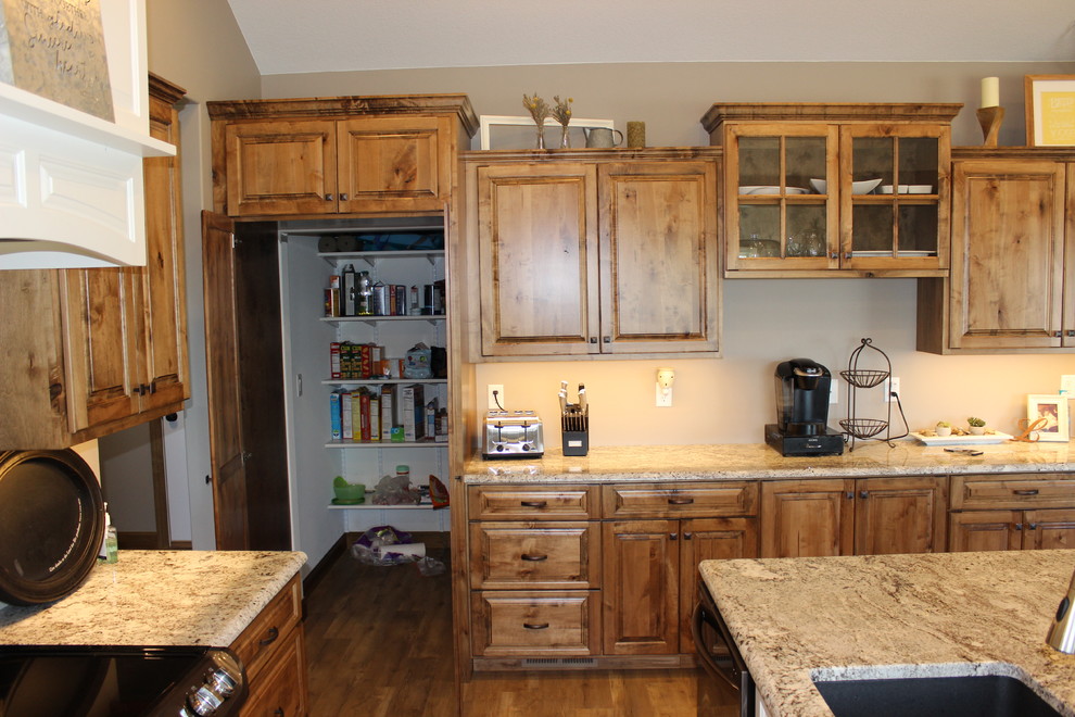 Large mountain style l-shaped medium tone wood floor and brown floor open concept kitchen photo with an undermount sink, raised-panel cabinets, medium tone wood cabinets, granite countertops, stainless steel appliances and an island