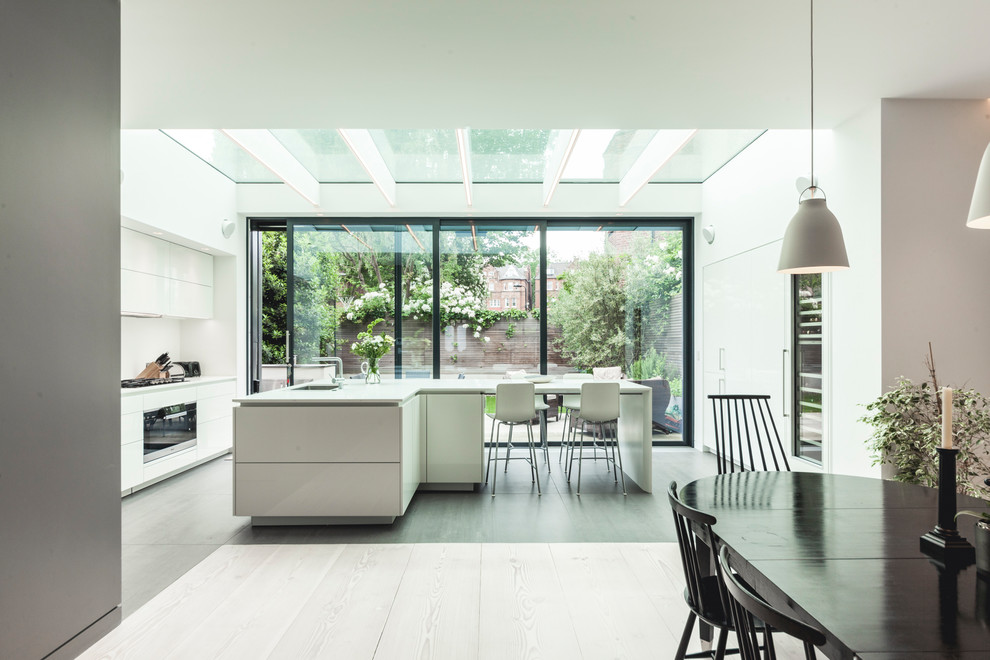 Expansive contemporary single-wall eat-in kitchen in London with flat-panel cabinets, white cabinets, stainless steel appliances, light hardwood floors, with island, grey floor and white benchtop.