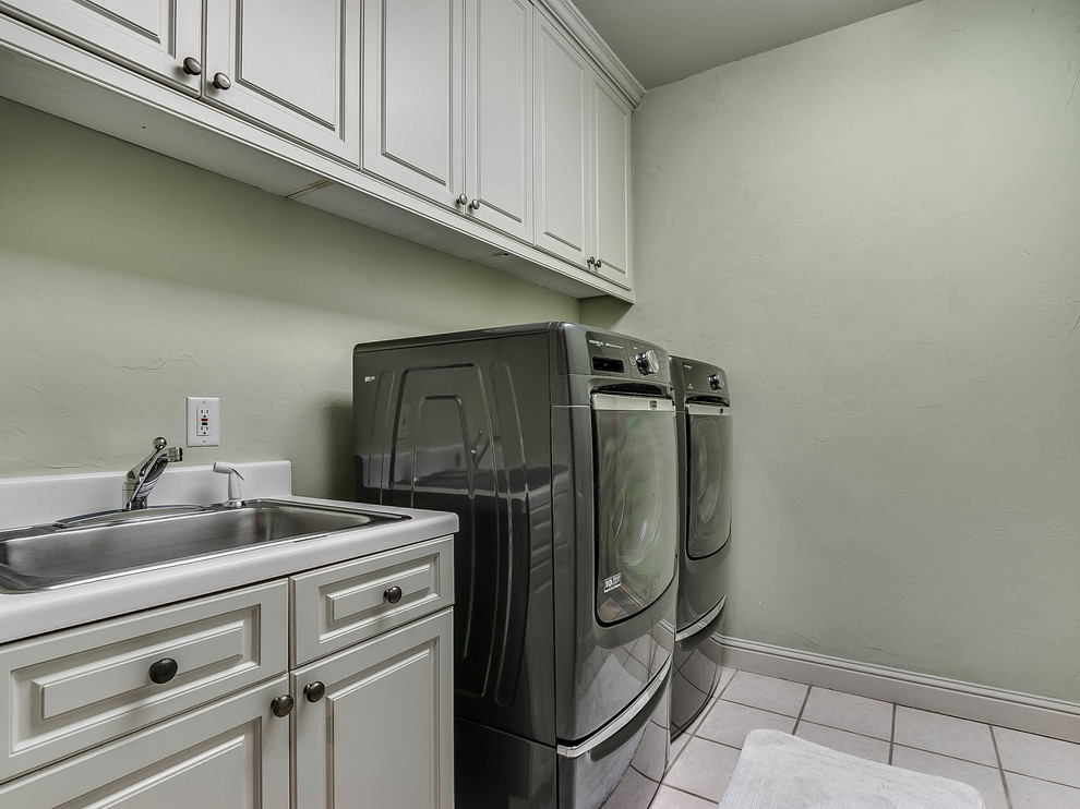 Inspiration for a mid-sized traditional single-wall dedicated laundry room in Oklahoma City with a drop-in sink, flat-panel cabinets, white cabinets, laminate benchtops, green walls, ceramic floors, a side-by-side washer and dryer and white floor.