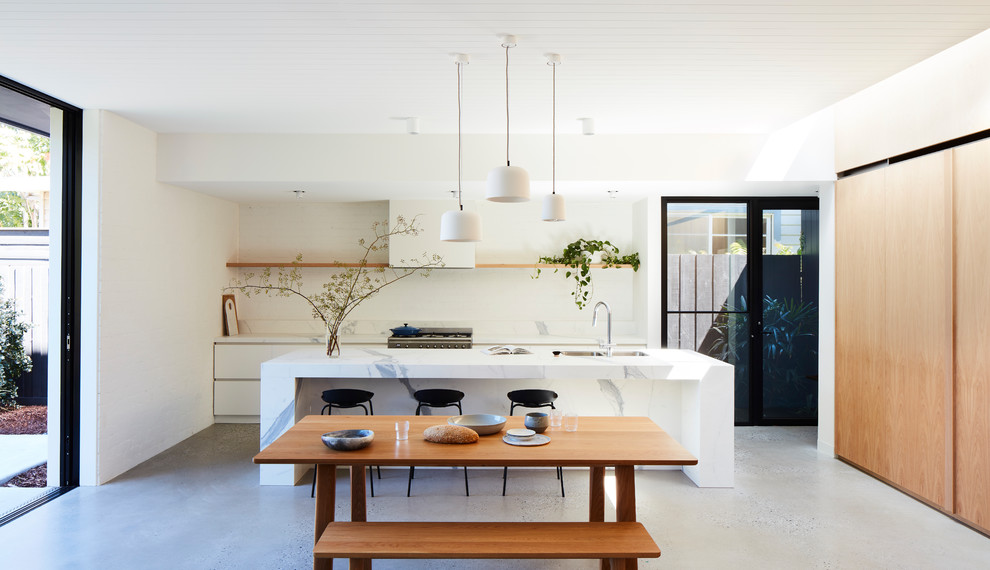 Inspiration for a large contemporary galley open plan kitchen in Melbourne with an undermount sink, white splashback, brick splashback, stainless steel appliances, concrete floors, with island, grey floor, white benchtop, flat-panel cabinets and white cabinets.