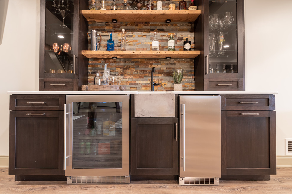 This is an example of a small country single-wall wet bar in Philadelphia with an undermount sink, flat-panel cabinets, dark wood cabinets, wood benchtops, multi-coloured splashback, stone tile splashback, laminate floors, brown floor and white benchtop.