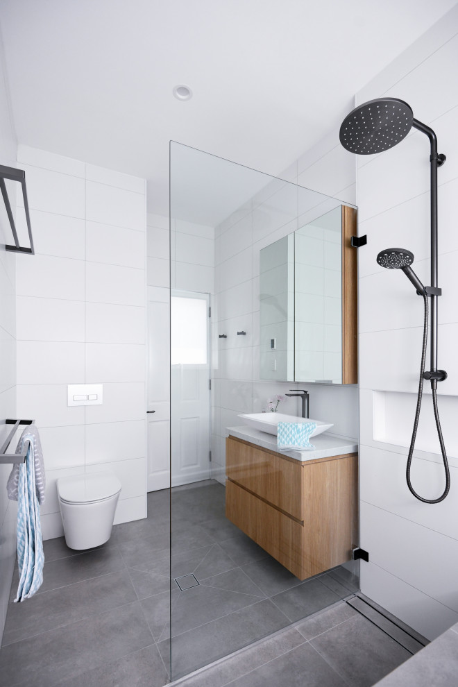Photo of a mid-sized scandinavian master wet room bathroom in Sydney with flat-panel cabinets, medium wood cabinets, a drop-in tub, a wall-mount toilet, white tile, ceramic tile, white walls, ceramic floors, a drop-in sink, engineered quartz benchtops, grey floor, an open shower and white benchtops.