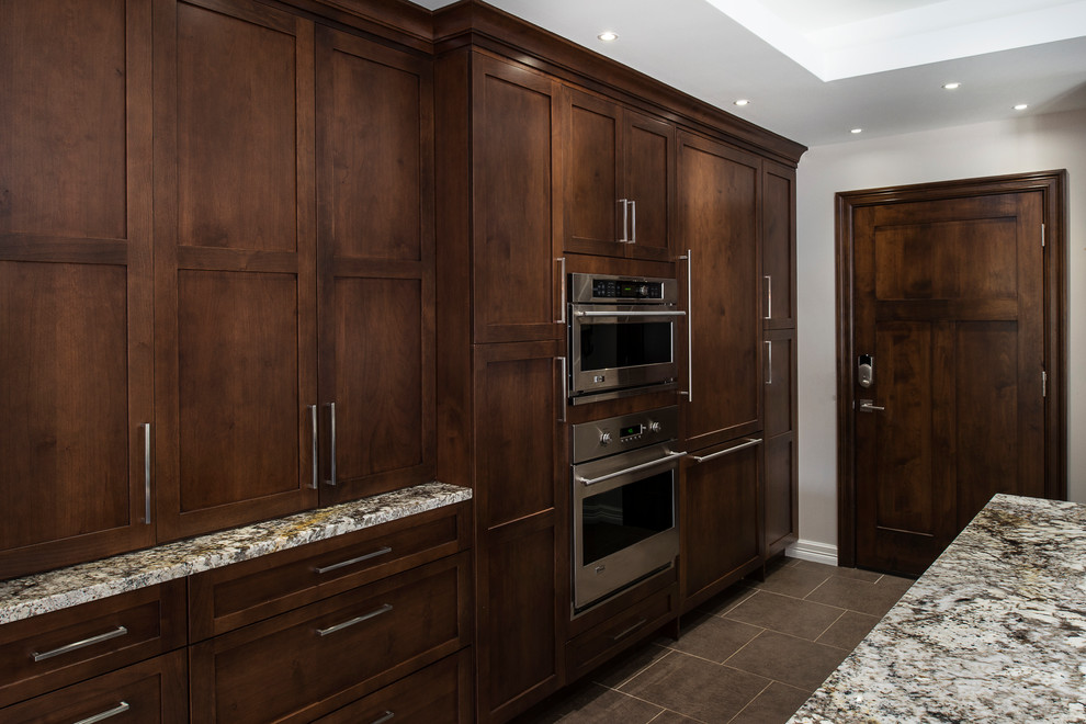 Inspiration for a large transitional ceramic tile and beige floor eat-in kitchen remodel with an undermount sink, shaker cabinets, brown cabinets, granite countertops, white backsplash, glass tile backsplash, stainless steel appliances and an island