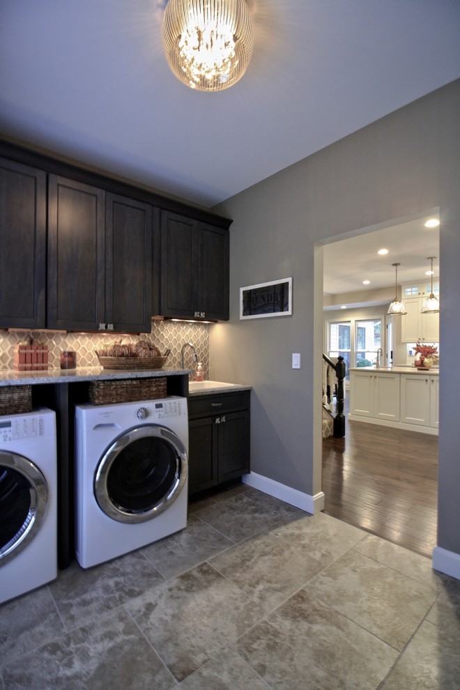 Design ideas for a mid-sized transitional single-wall utility room with recessed-panel cabinets, medium wood cabinets, quartz benchtops, grey walls, porcelain floors, a side-by-side washer and dryer, grey floor and a drop-in sink.