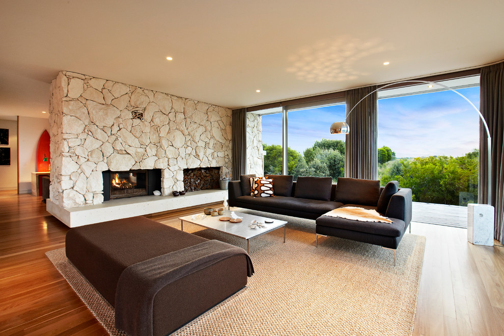Photo of a large midcentury formal open concept living room in Melbourne with medium hardwood floors, a standard fireplace and a stone fireplace surround.