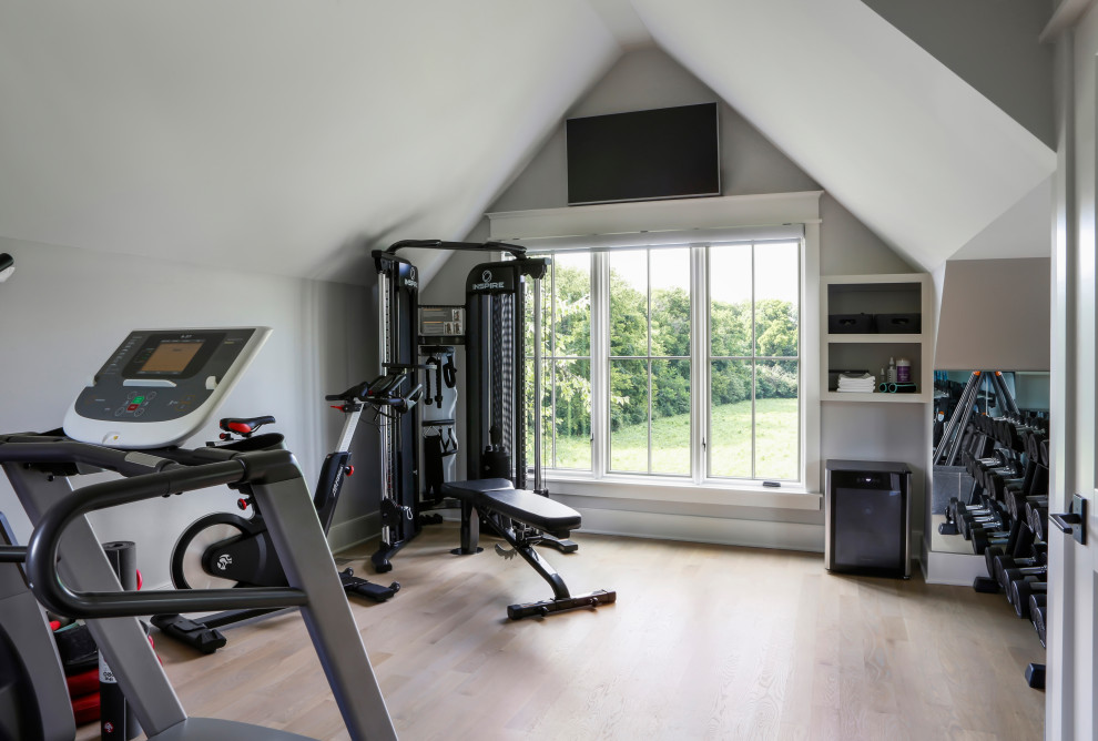 Imagen de sala de pesas de estilo de casa de campo grande con paredes grises, suelo de madera en tonos medios y suelo marrón