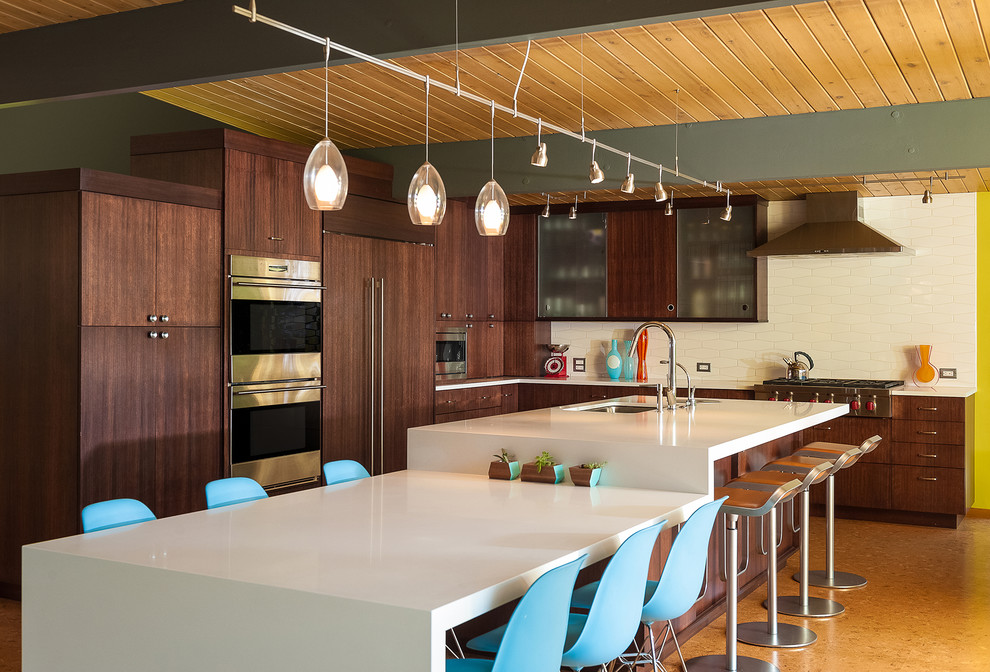 Photo of a midcentury l-shaped kitchen in Portland with an undermount sink, flat-panel cabinets, dark wood cabinets, white splashback, panelled appliances, with island and white benchtop.