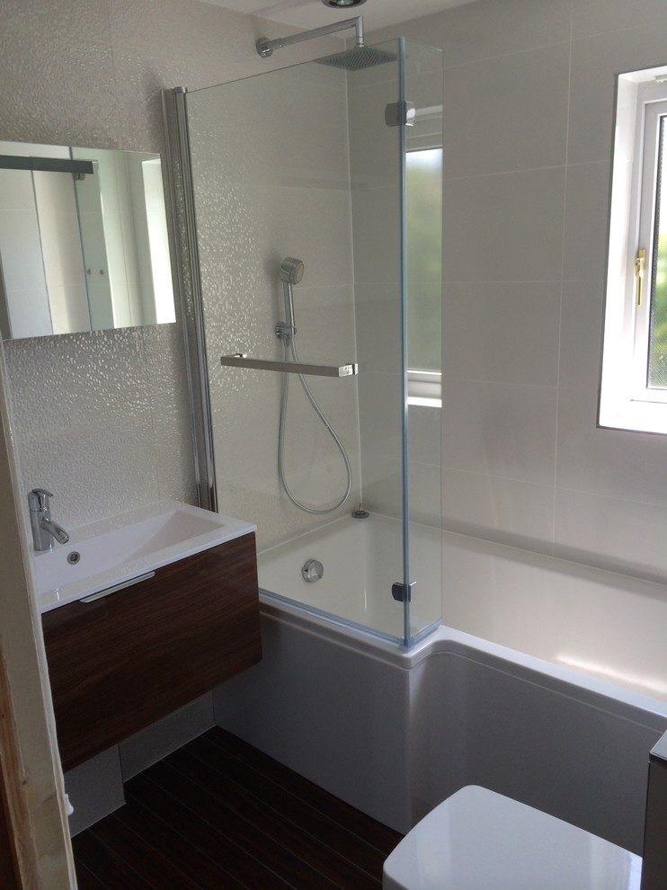 This is an example of a mid-sized contemporary bathroom in Essex with a wall-mount sink, flat-panel cabinets, medium wood cabinets, wood benchtops, a two-piece toilet, white tile, ceramic tile, white walls and linoleum floors.