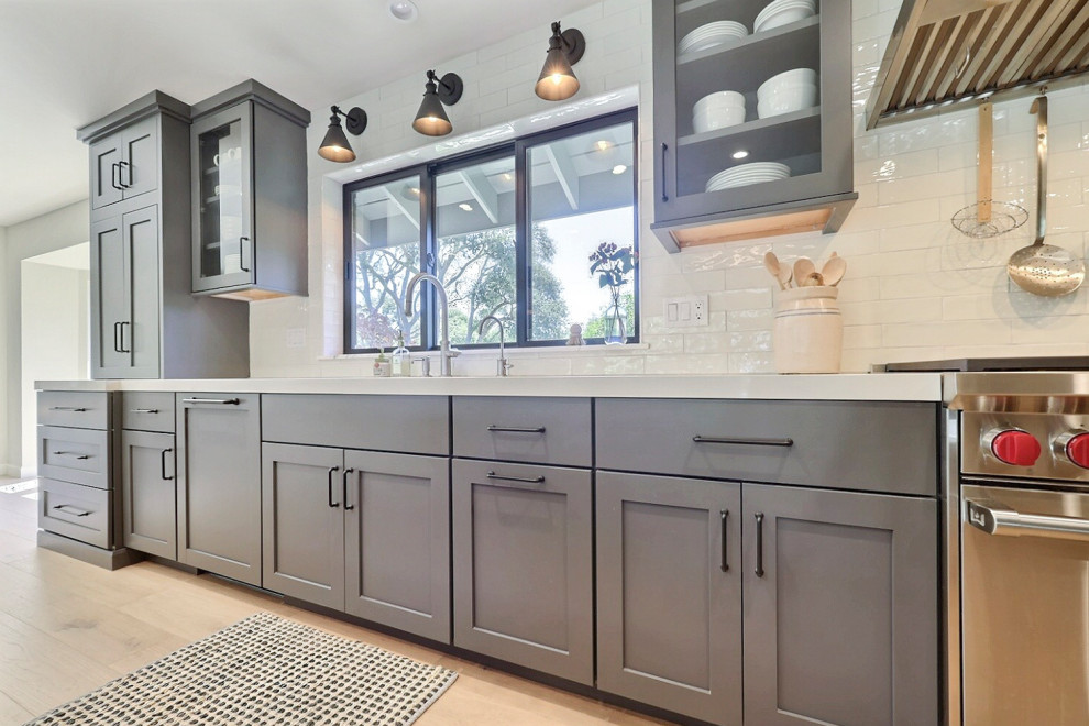 Mid-sized transitional l-shaped laminate floor open concept kitchen photo with a double-bowl sink, flat-panel cabinets, gray cabinets, quartz countertops, white backsplash, ceramic backsplash, stainless steel appliances, an island and white countertops